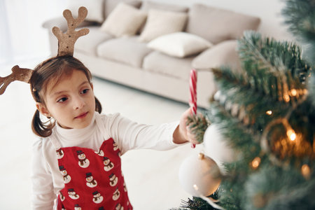 Cute little girl standing new New year tree with candy in handの写真素材