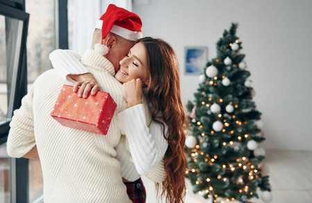 Girls holds red gift box. Young romantic couple celebrates New year together indoorsの写真素材