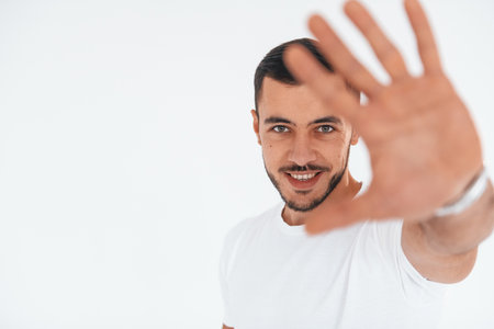 Stop gesture. Young handsome man standing indoors against white backgroundの写真素材