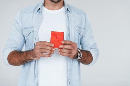 With red gift box. Close up particle view of young man that standing indoors against white backgroundの写真素材