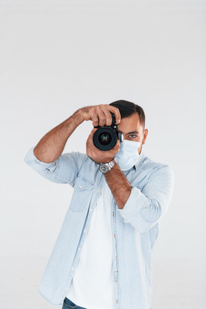 With professional camera. Young handsome man standing indoors against white backgroundの写真素材