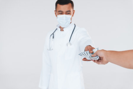 Medic holds money. Young handsome man standing indoors against white backgroundの写真素材
