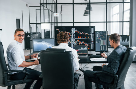 Conception of teamwork. Team of stockbrokers works in modern office with many display screens