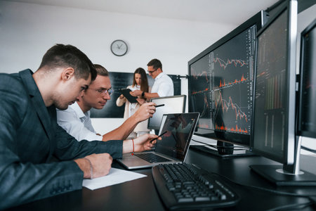 Attention to details. Team of stockbrokers works in modern office with many display screensの写真素材