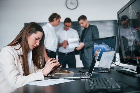 Woman sits in front of laptop and displays. Team of stockbrokers works in modern office with many display screensの写真素材