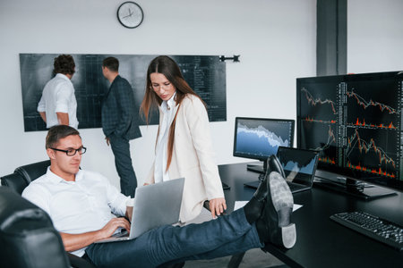 Woman and man have conversation. Team of stockbrokers works in modern office with many display screensの写真素材