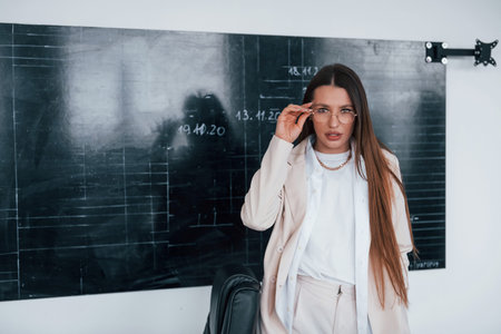 Young smart woman with glasses standing near blackboard