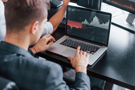 Man uses laptop. Team of stockbrokers works in modern office with many display screensの写真素材
