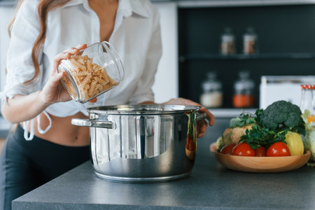 Preparation of meal in bowl. Young european woman is indoors at kitchen indoors with healthy foodの写真素材