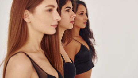 Side view. Three young women in lingerie together indoors. White background