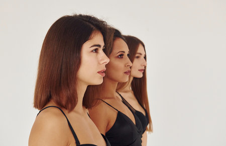 Side view. Three young women in lingerie together indoors. White backgroundの写真素材