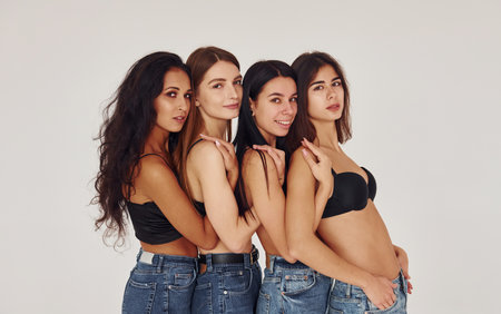 Leaning on each other. Four young women in lingerie together indoors. White backgroundの写真素材