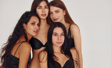 Leaning on each other. Four young women in lingerie together indoors. White backgroundの写真素材