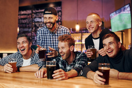 Football fans watching TV. Group of people together indoors in the pub have fun at weekend timeの写真素材