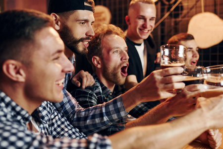 Fans cheer and shout. Group of people together indoors in the pub have fun at weekend timeの写真素材