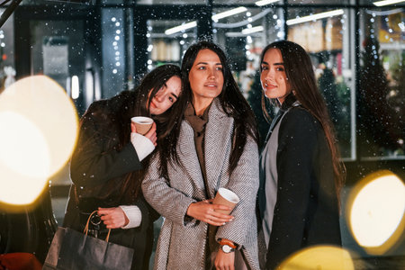 Cups of drink in hands. Three cheerful women spends Christmas holidays together outdoors. Conception of new yearの写真素材