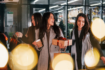 Cups of drink in hands. Three cheerful women spends Christmas holidays together outdoors. Conception of new yearの写真素材