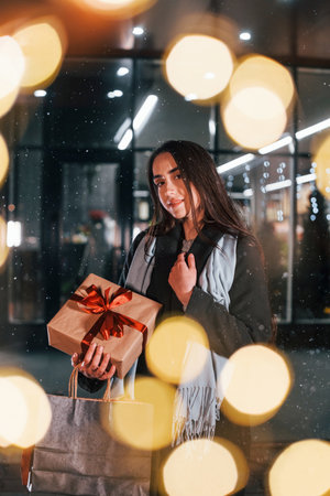 From the shop with gift box in hands. Cheerful woman is outdoors at Christmas holidays time. Conception of new yearの写真素材
