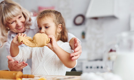 Kneads the dough. Senior grandmother with her little granddaughter cooks sweets for Christmas on the kitchenの写真素材