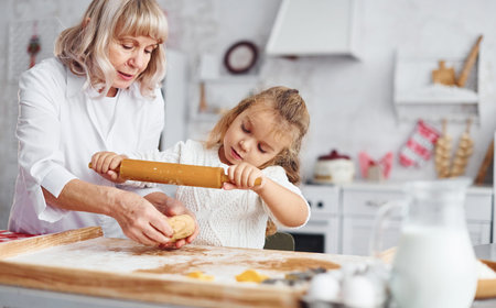 Kneads the dough. Senior grandmother with her little granddaughter cooks sweets for Christmas on the kitchenの写真素材