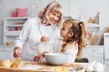 Fills with milk. Senior grandmother with her little granddaughter cooks sweets for Christmas on the kitchenの写真素材