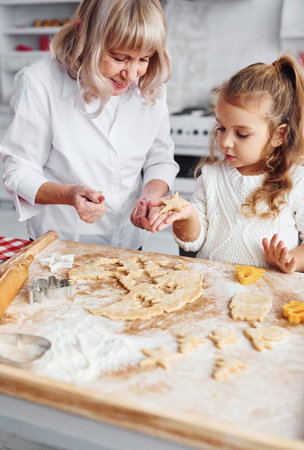 Teaching process. Senior grandmother with her little granddaughter cooks sweets for Christmas on the kitchenの写真素材