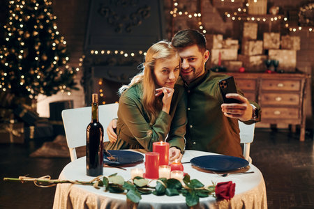 Making selfie by using phone. Young lovely couple have romantic dinner indoors togetherの写真素材