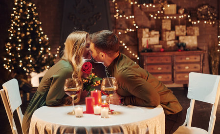 Holding beautiful red rose. Young lovely couple have romantic dinner indoors togetherの写真素材