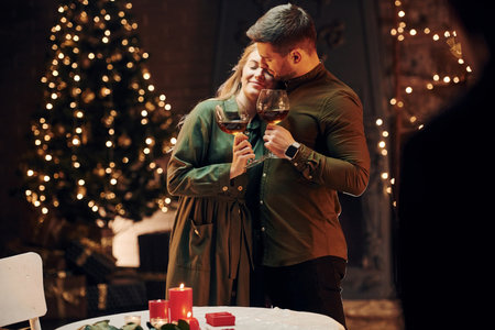Standing and holding big glasses with wine. Young lovely couple have romantic dinner indoors togetherの写真素材