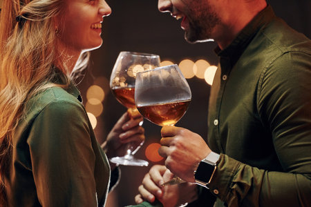 Standing and holding big glasses with wine. Young lovely couple have romantic dinner indoors togetherの写真素材