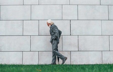 Senior businessman in formal clothes, with grey hair and beard is outdoors walks with umbrella in handの写真素材