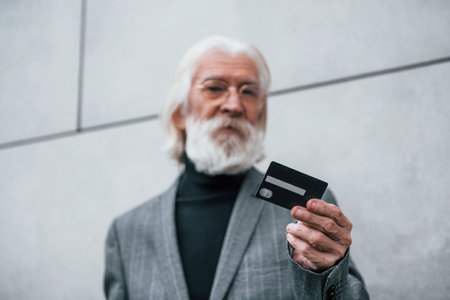 Senior businessman in formal clothes, with grey hair and beard is outdoors holds credit cardの写真素材
