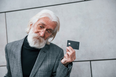 Senior businessman in formal clothes, with grey hair and beard is outdoors holds credit cardの写真素材