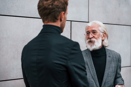 Having a meet. Young guy with senior man in elegant clothes is outdoors together. Conception of businessの写真素材