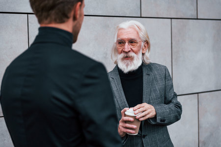 Having a meet. Young guy with senior man in elegant clothes is outdoors together. Conception of businessの写真素材