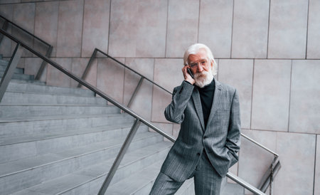 Senior businessman in formal clothes, with grey hair and beard is outdoors talks by phoneの写真素材
