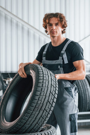 Holds tire. Adult man in grey colored uniform works in the automobile salonの写真素材
