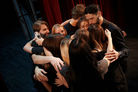 Embracing each other. Group of actors in dark colored clothes on rehearsal in the theaterの写真素材