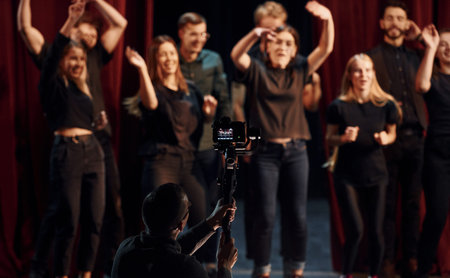 Happy people celebrating success. Group of actors in dark colored clothes on rehearsal in the theaterの写真素材