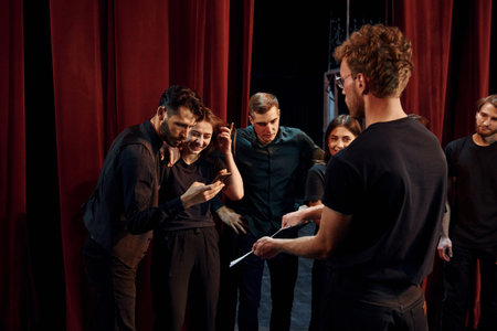 Man with notepad practice his role. Group of actors in dark colored clothes on rehearsal in the theaterの写真素材