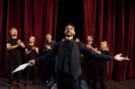 Expressionalible guy practicing his role. Group of actors in dark colored clothes on rehearsal in the theaterの写真素材