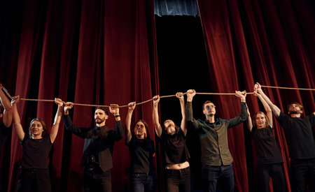 Holding rope in hands above the heads. Group of actors in dark colored clothes on rehearsal in the...