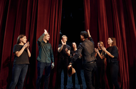 Standing against red curtains. Group of actors in dark colored clothes on rehearsal in the theaterの写真素材