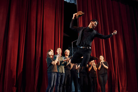 Standing against red curtains. Group of actors in dark colored clothes on rehearsal in the theaterの写真素材