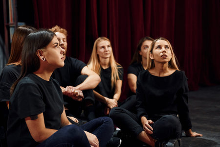 Sitting on the floor. Group of actors in dark colored clothes on rehearsal in the theater