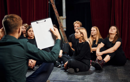 Sitting on the floor. Group of actors in dark colored clothes on rehearsal in the theaterの写真素材