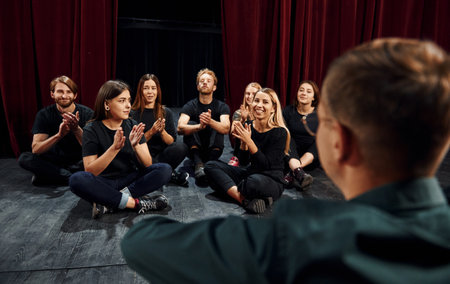 Sitting on the floor. Group of actors in dark colored clothes on rehearsal in the theaterの写真素材