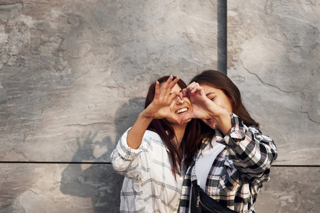 Love gesture. Beautiful cheerful friends or lesbian couple together near wall outdoors at daytimeの写真素材