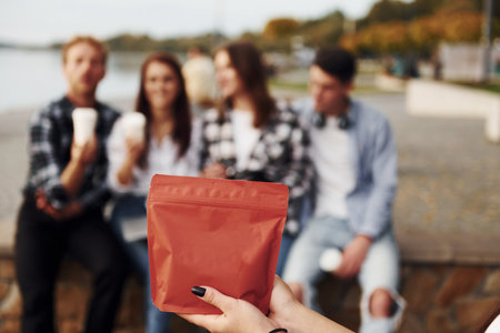 Red package of coffee. Group of young cheerful friends that is outdoors having fun togetherの写真素材
