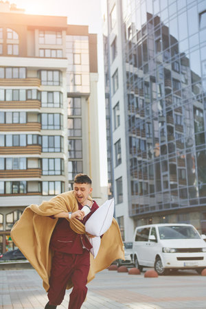 Running, late for the work. Young man in pajama is outdoors on the street. Feels sleepyの写真素材